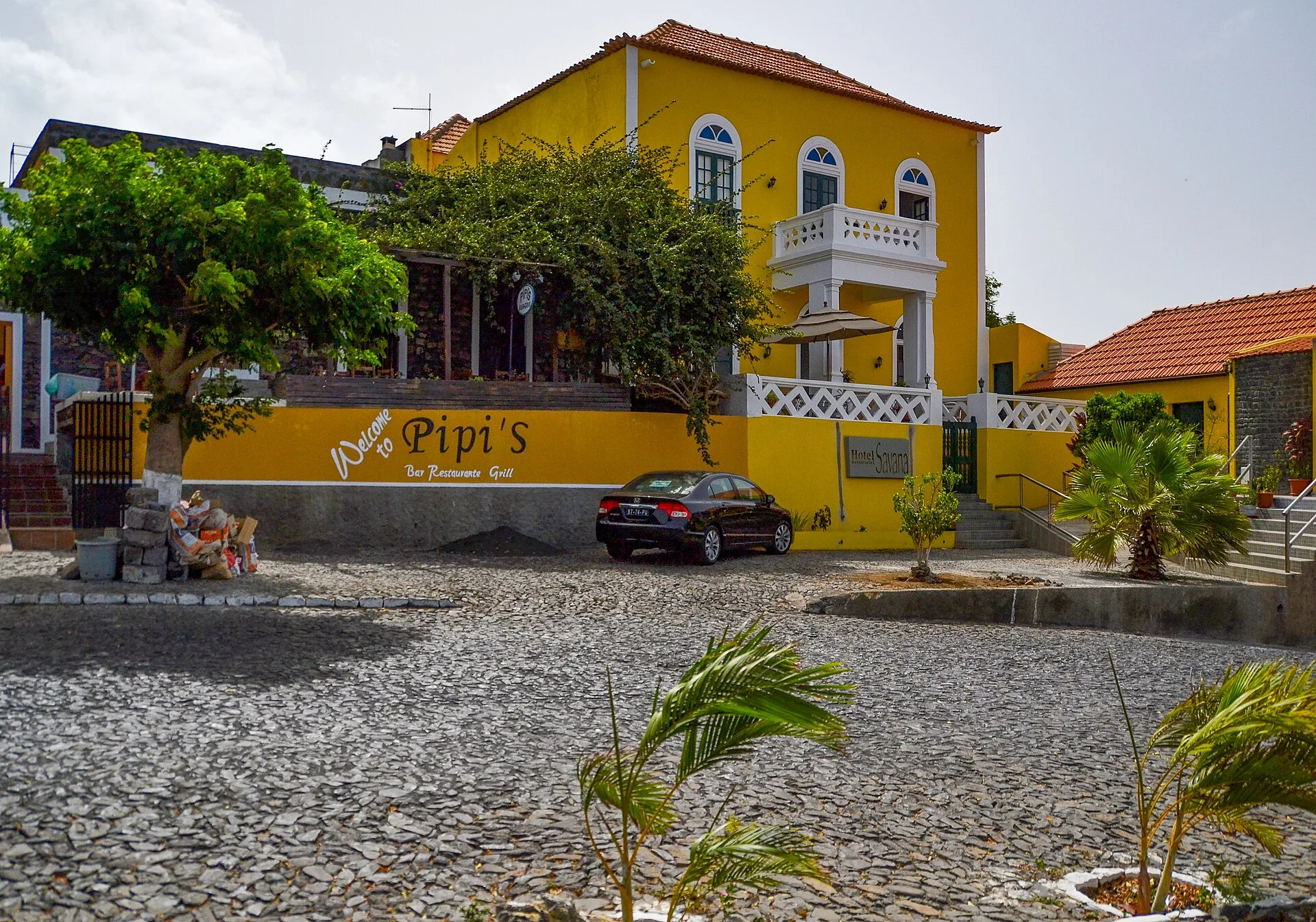 Façade jaune d'un hôtel et restaurant à balcon blanc sur une place pavée de São Filipe, Fogo, Cap-Vert