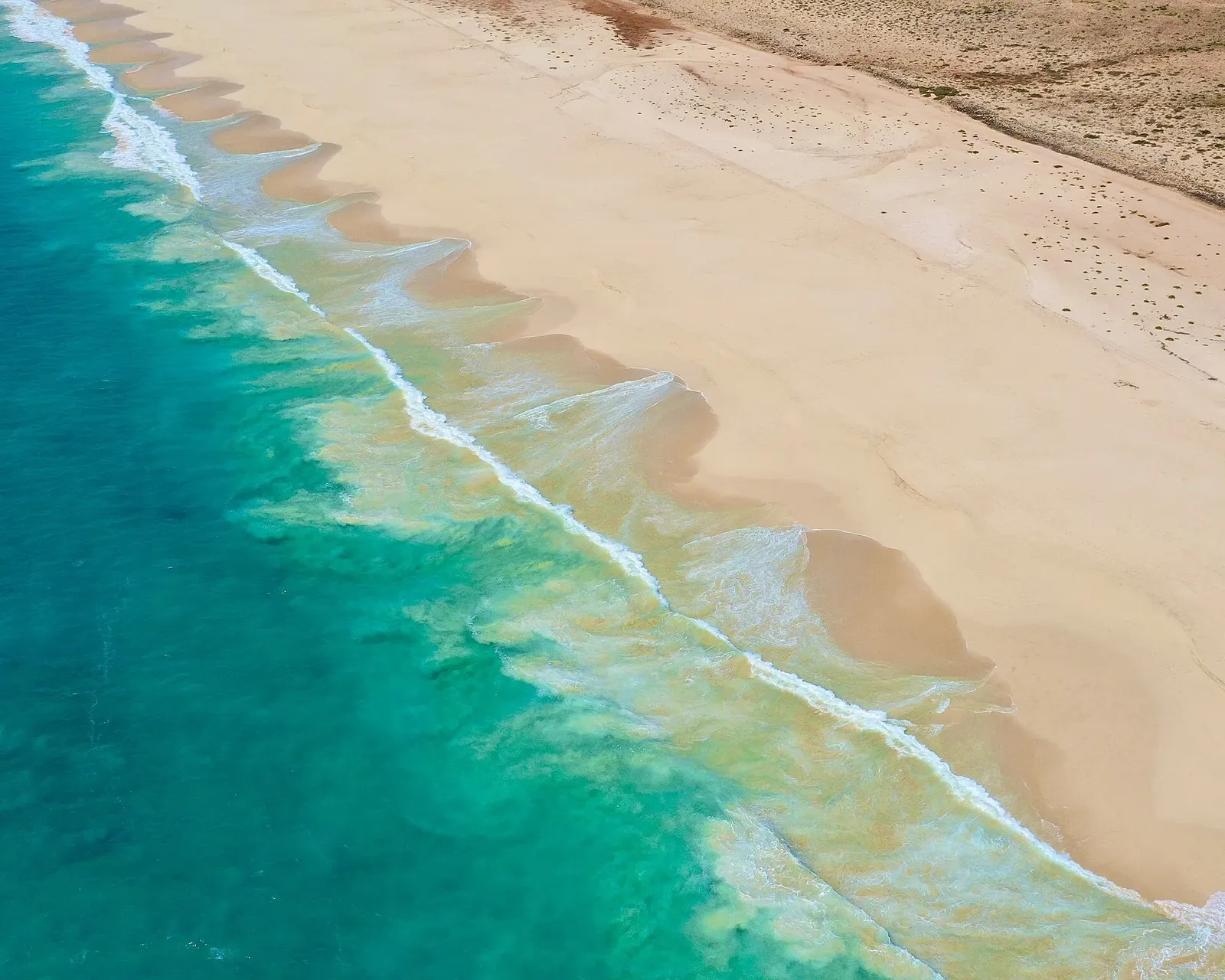 Vue aérienne d'une longue plage de sable clair bordée par une mer turquoise et des vagues écumeuses