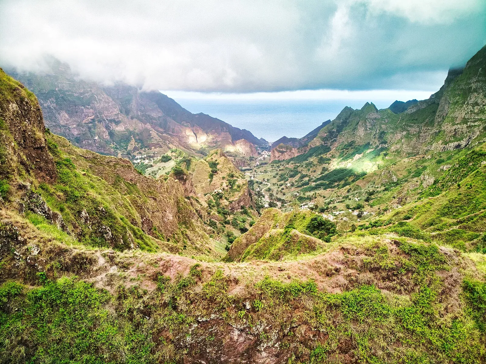 Vallée verdoyante aux crêtes escarpées, ouverte sur l'océan Atlantique sous les nuages, vue depuis Pico da Cruz
